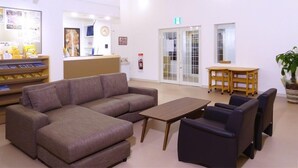 A reception area with a sofa, chairs, a small table, and a wooden table with chairs. There is a fire extinguisher on the wall and a clock. - Family Lodge Hatagoya Kobe Suma (Kobe)
