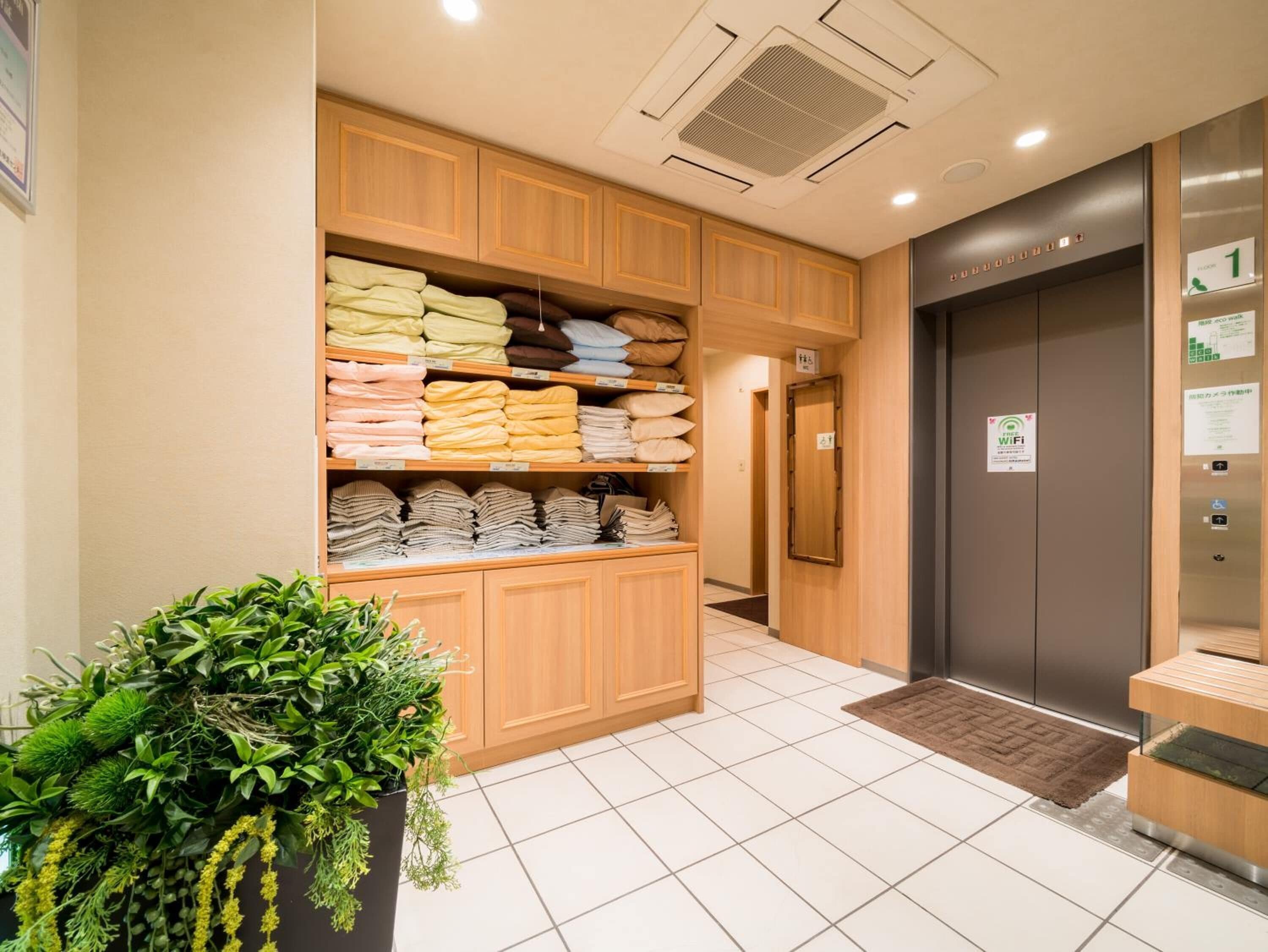 A hotel lobby with a reception area, a plant, and a wall with neatly stacked towels and robes.