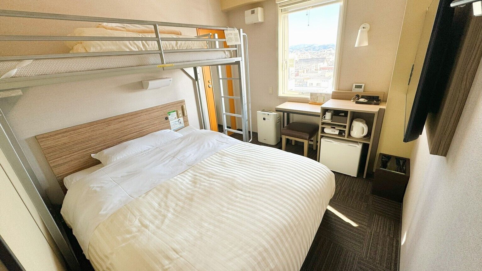 A bunk bed room with a desk, chair, and window with a city view.