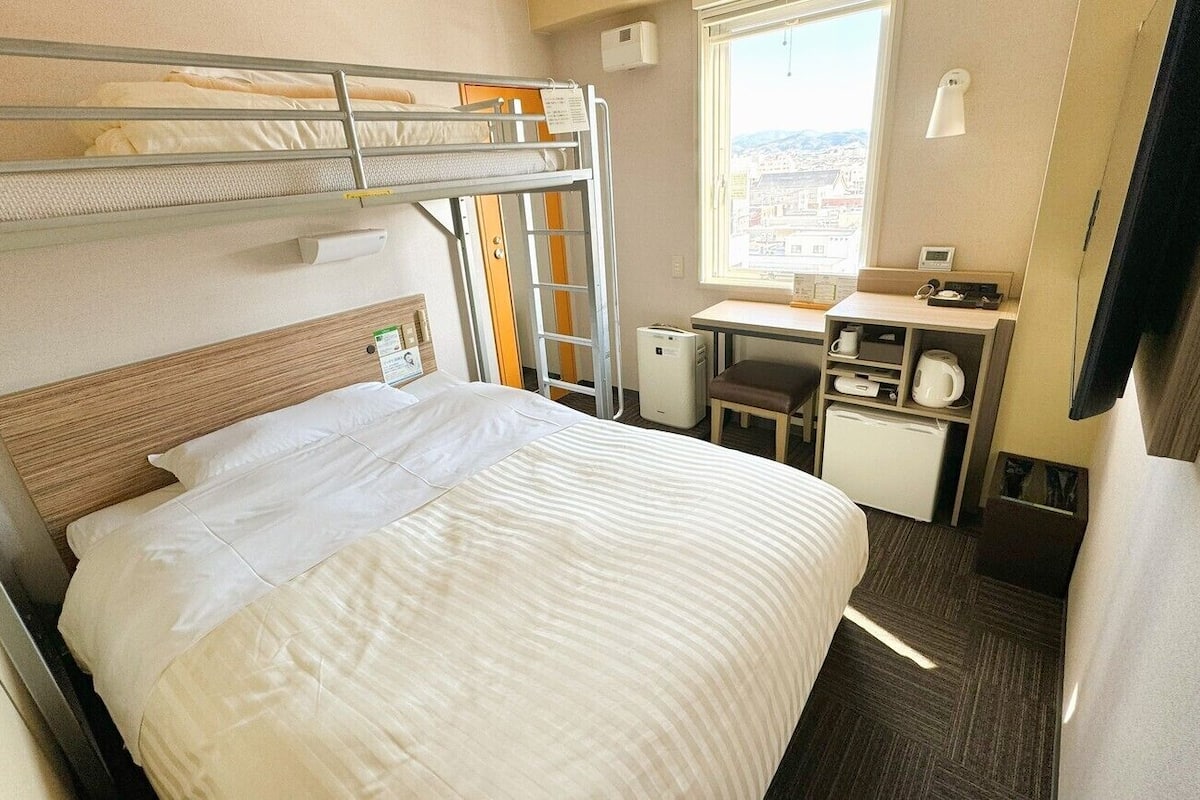 A bunk bed room with a desk, chair, and window with a city view.