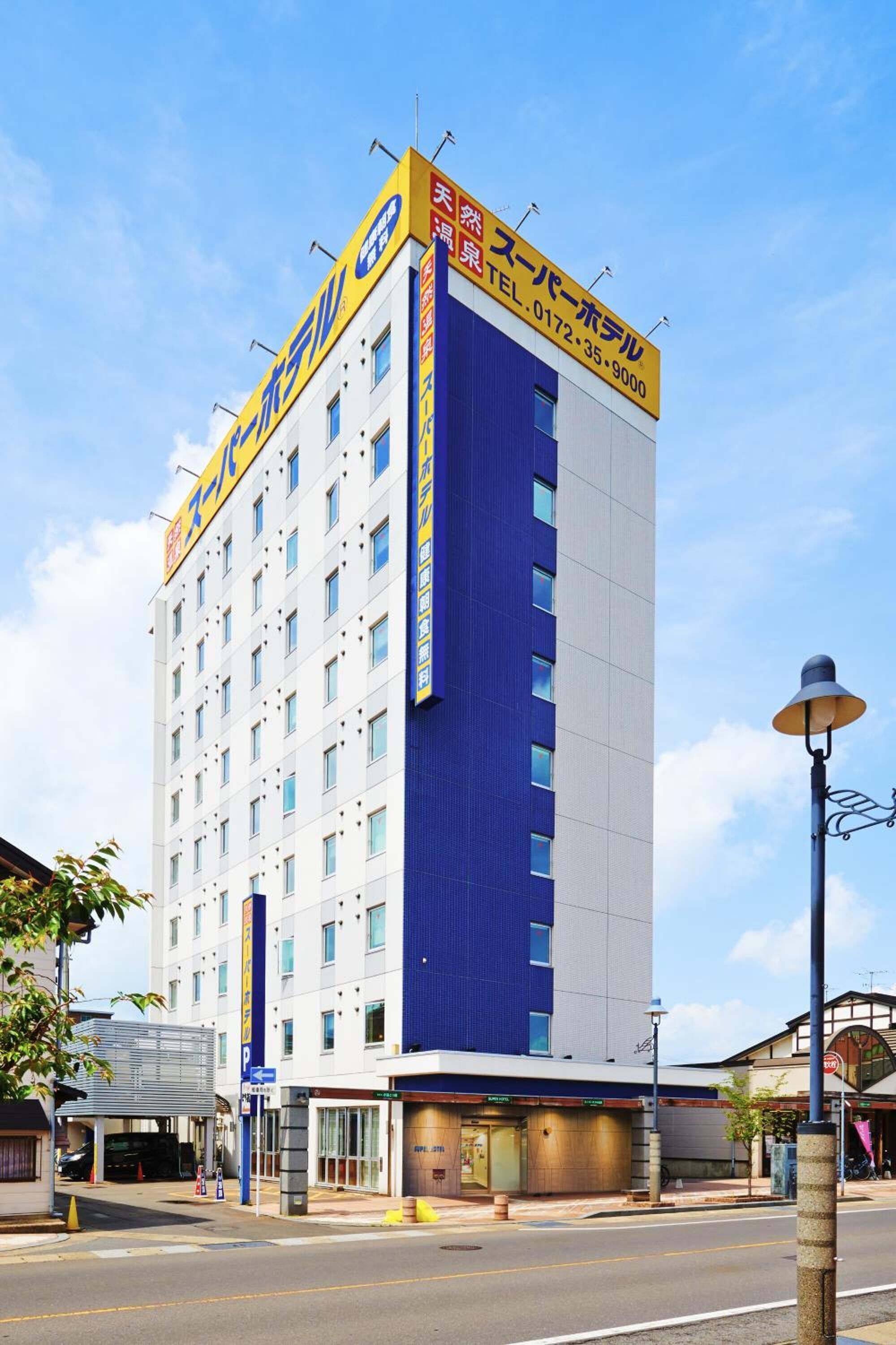 A multi-story hotel with a prominent blue and white facade, a visible entrance, and a signboard with contact information.