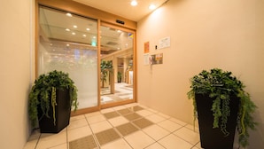 A hotel entrance with a tiled floor, a glass door, and two potted plants. - Super Hotel Hirosaki (Hirosaki)