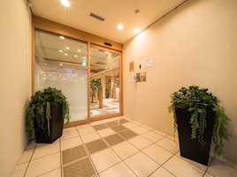 A hotel entrance with a tiled floor, a glass door, and two potted plants.
