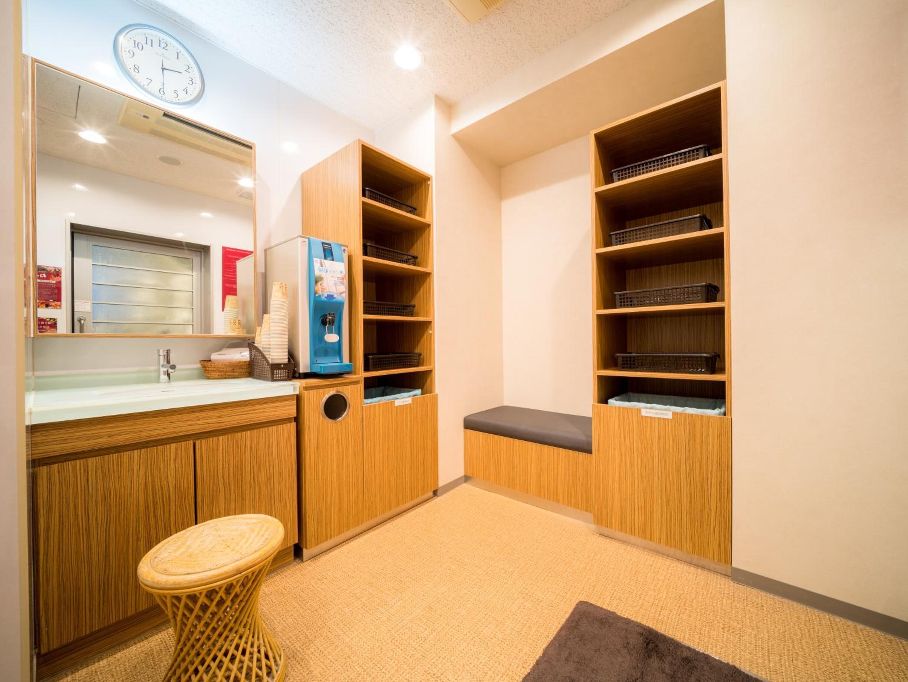 A hotel room with a wooden cabinet, a small stool, a water dispenser, and a clock on the wall.