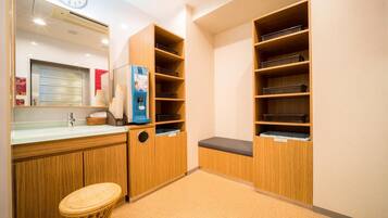 A hotel room with a wooden cabinet, a small stool, a water dispenser, and a clock on the wall.