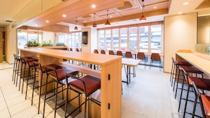 A spacious dining area with long wooden tables and metal chairs, large windows with a view of the street, and a modern ceiling design. - Super Hotel Hirosaki (Hirosaki)