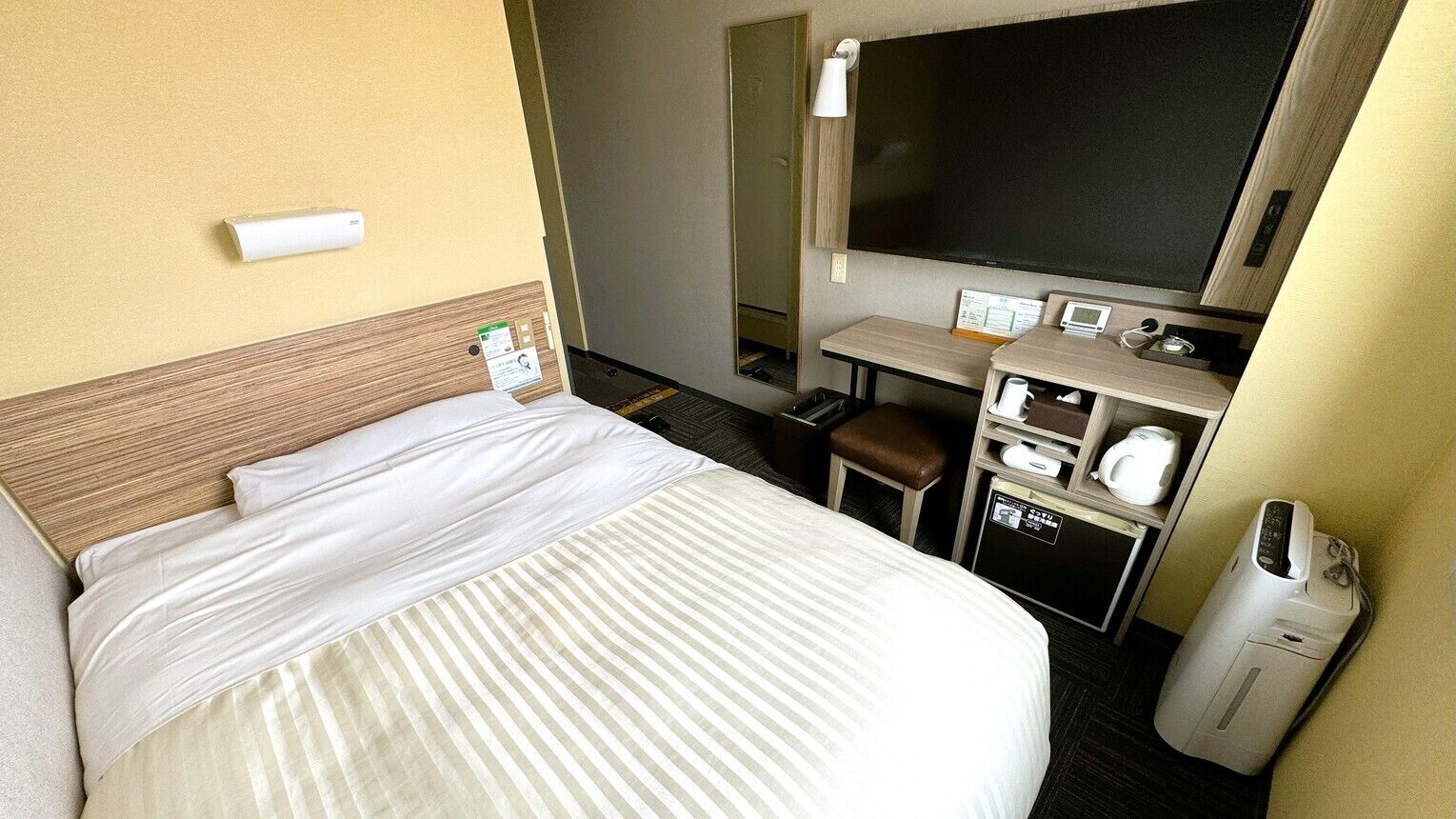 A hotel room with a bed, a desk, a chair, a TV, and a minibar.