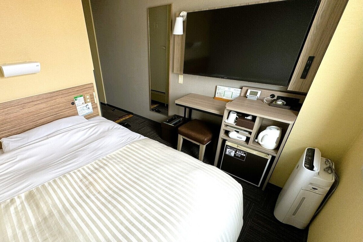 A hotel room with a bed, a desk, a chair, a TV, and a minibar.