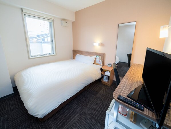 Habitación de hotel con cama, escritorio con computadora y televisor, mesita de noche, espejo y ventana.