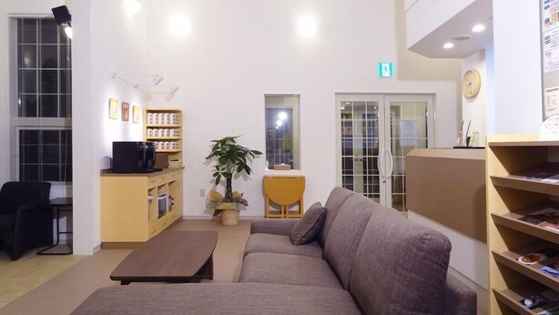 A reception area with a sofa, coffee table, and a small desk with a computer. There are shelves with books and a potted plant. - Family Lodge Hatagoya Meihan Nagashima (Kuwana)
