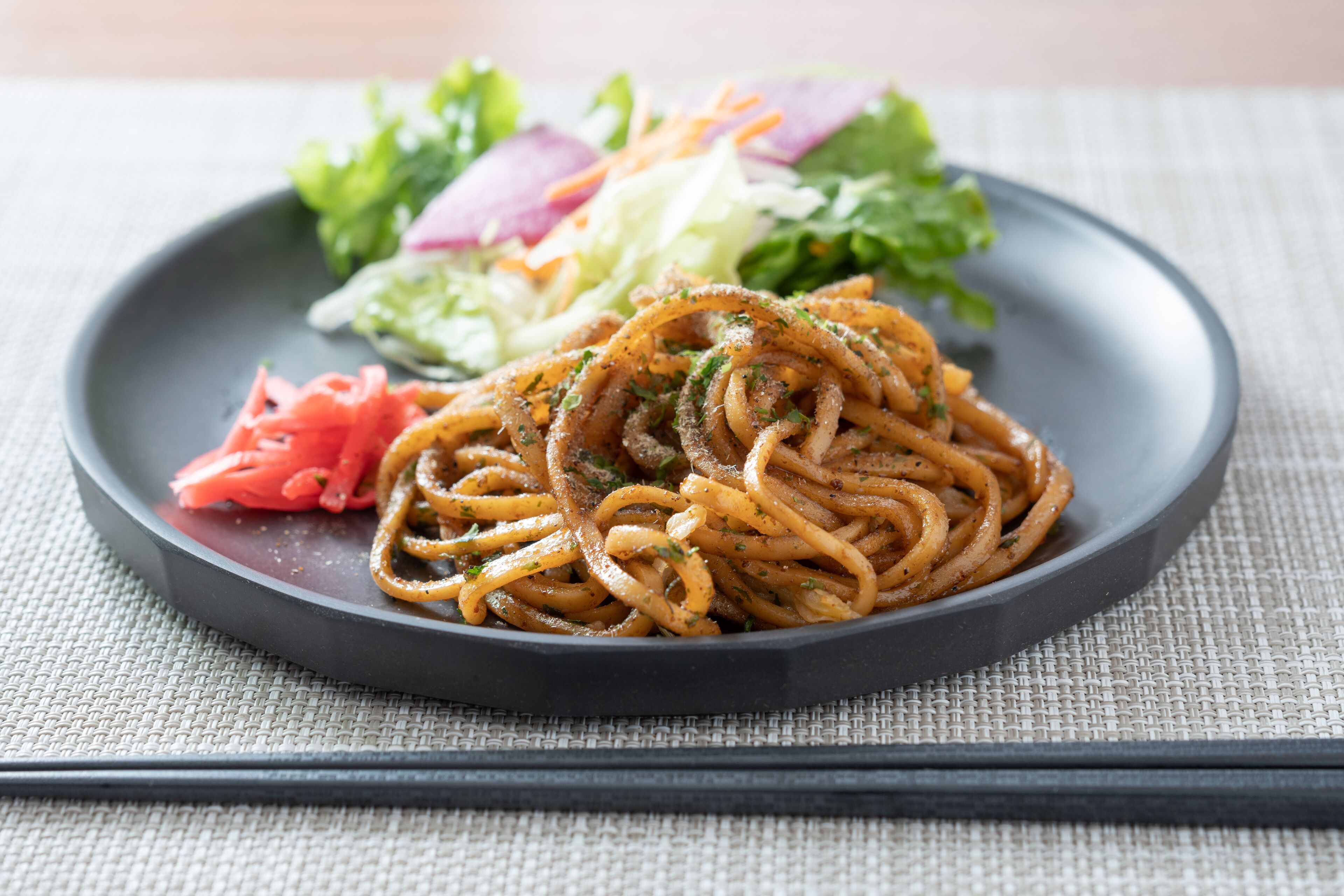 A plate of spaghetti with a side salad and carrot slaw.