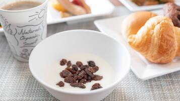 Une table mise pour le petit-déjeuner, avec un bol de yaourt et de raisins secs, un croissant et une tasse de café.