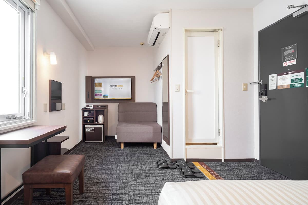 Habitació d'hotel amb llit, escriptori, cadira, petita cuineta i porta.