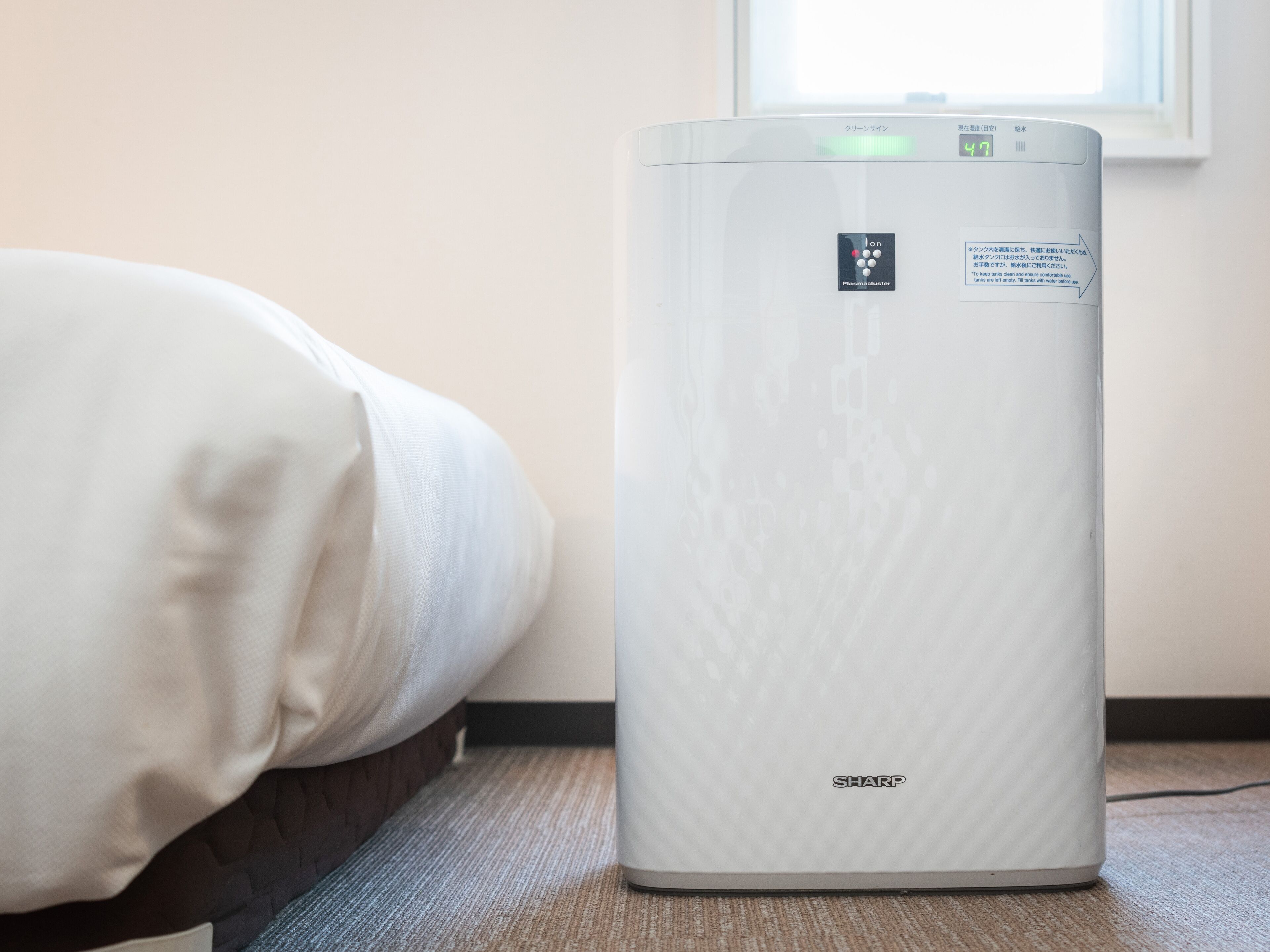 A room with a bed, a white air purifier, and a window.