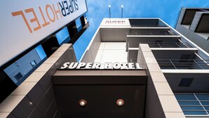 Un moderno edificio de hotel con un llamativo letrero de 'SuperHotel', varios pisos y un cielo despejado.