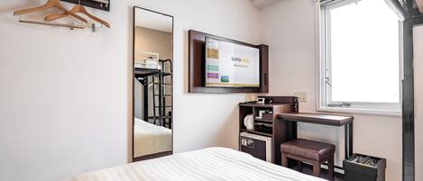A hotel room with a bed, a desk with a computer, a mirror, a TV, and a window.