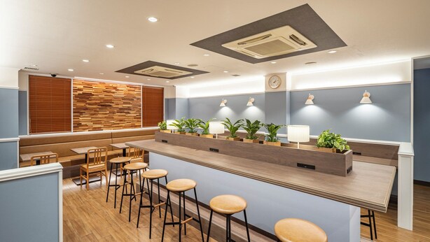 Zona de bar moderna con taburetes de madera, una barra larga e iluminación ambiental.