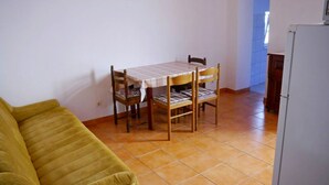 A small dining area with a table and two chairs, a green sofa, and a white refrigerator. - Cosy Apartment With sea View and one Bedroom (Novalja)
