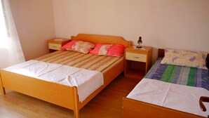 A room with two wooden beds, one with a striped bedspread and the other with a quilt. There are bedside tables with lamps and a small drawer. - Cosy Apartment With sea View and one Bedroom (Novalja)