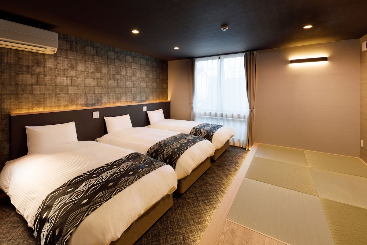 A hotel room with three beds, a large window with curtains, and a textured wall.