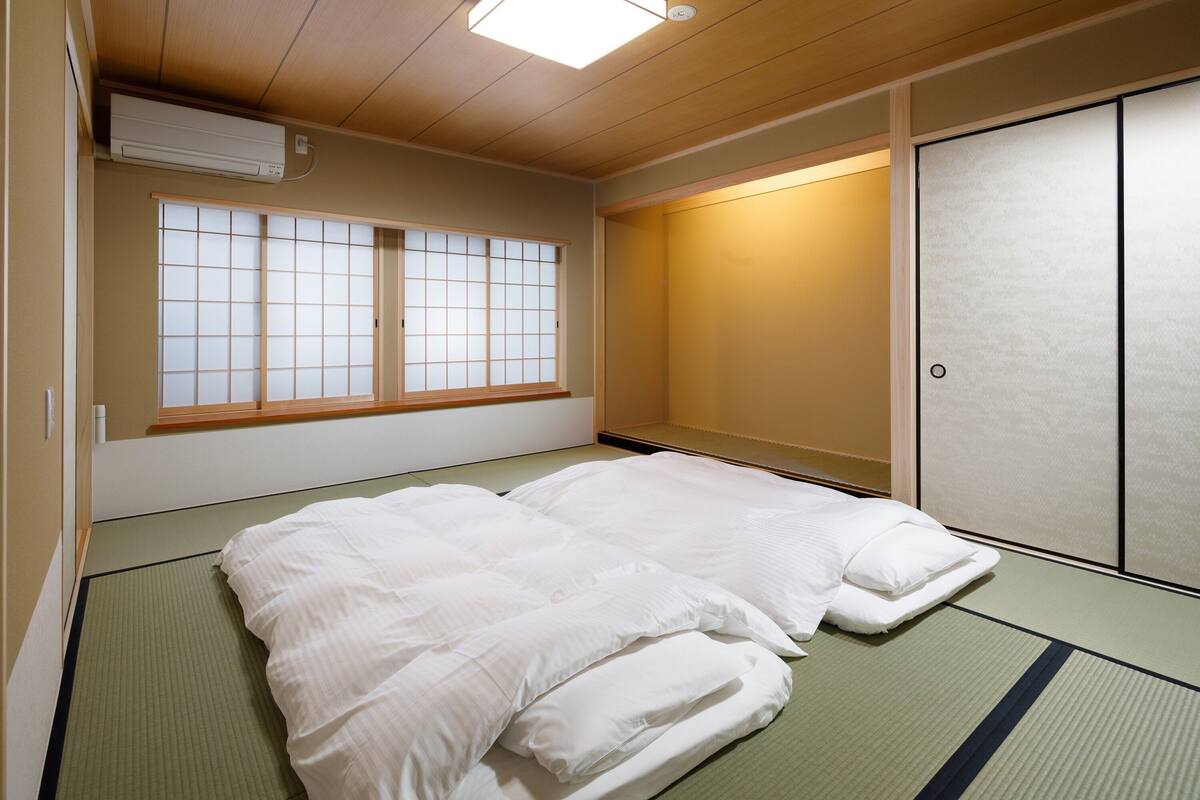 A room with tatami mat flooring, a futon bed, sliding shoji doors, and a window with a grid pattern.
