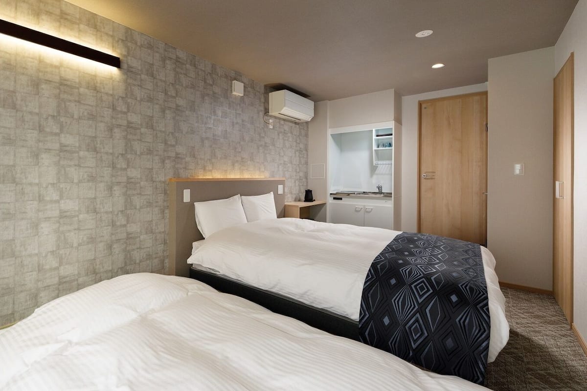 A hotel room with a large bed, a bedside table, an air conditioning unit, a mirror, and a wardrobe.