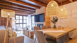 Àmplia zona d'estar amb una taula de dinar de fusta, cadires modernes i una llar de foc.