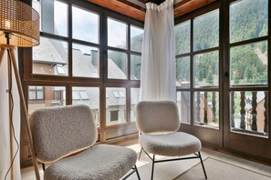 A room with large windows, two plush chairs, and a wooden ceiling.