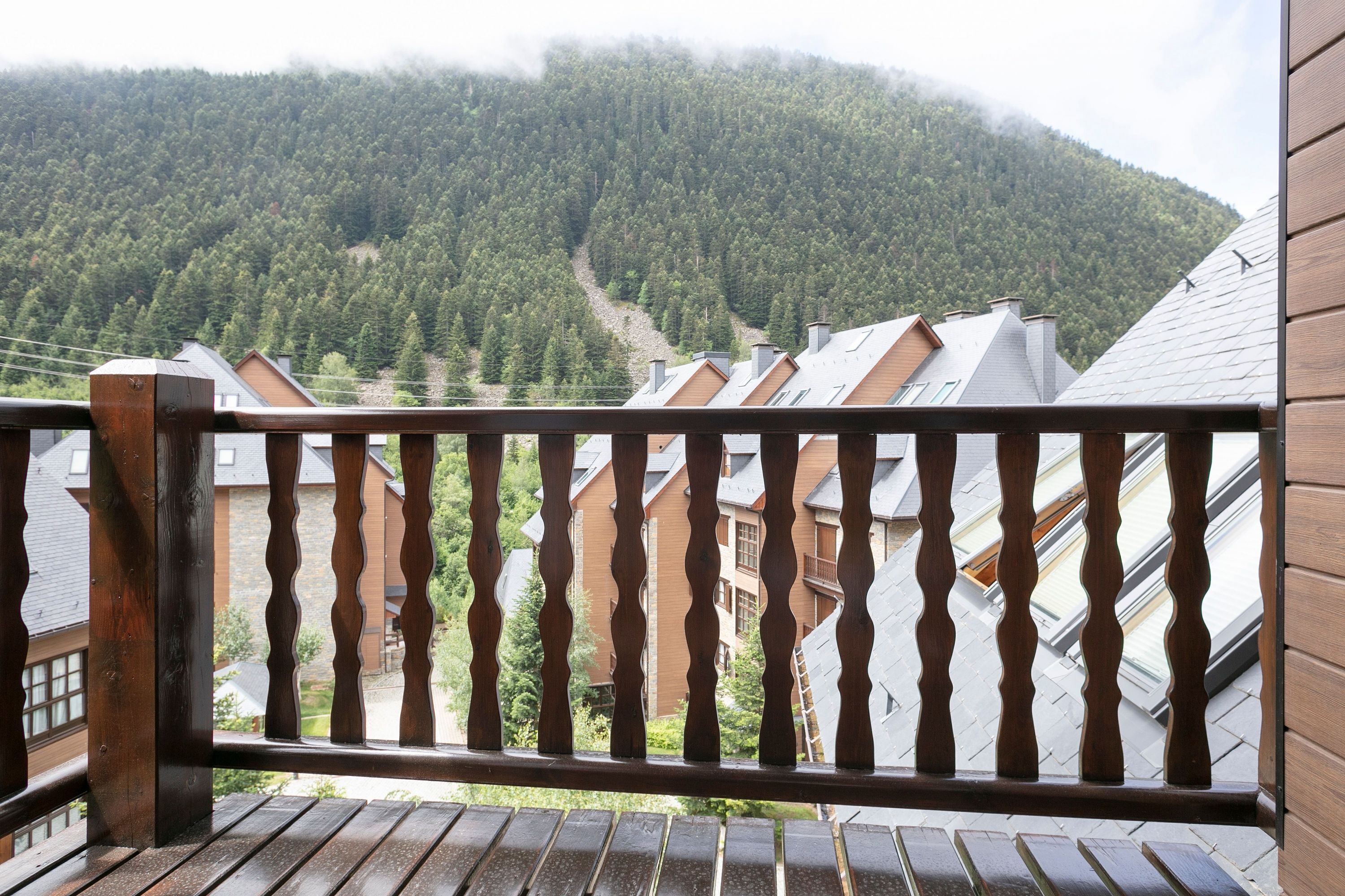 A wooden balcony railing overlooking a mountain with residential buildings.