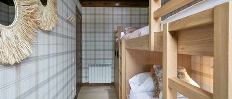 A narrow hallway with a checkered floor, wooden bunk beds, and a radiator.