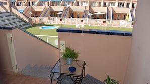 A balcony with a small table, potted plants, and a view of a swimming pool and building. - Lovely House Near to the sea (La Oliva)