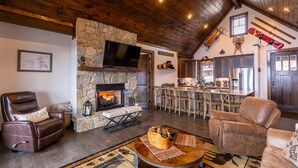 A cozy living room with a stone fireplace, leather sofas, a bar area, and a kitchen visible through an open door. - Green Valley III at Eagles Nest, amazing views! (Banner Elk)