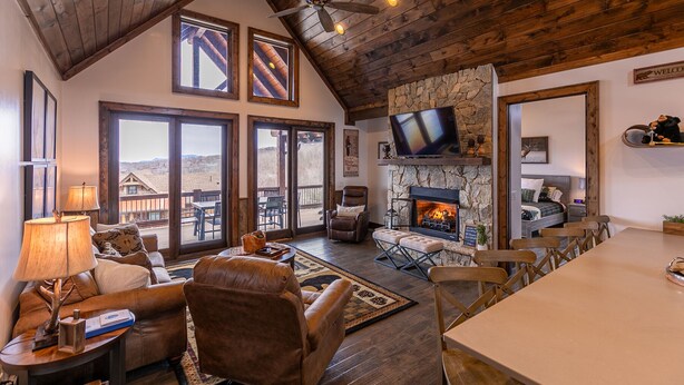 A spacious living area with a stone fireplace, large windows, and a ceiling fan. - Green Valley III at Eagles Nest, amazing views! (Banner Elk)