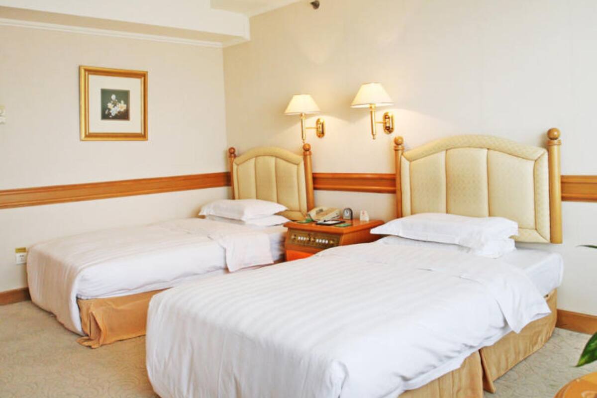 A hotel room with two beds, a wooden headboard, bedside lamps, a framed picture on the wall, and a small table with a telephone.
