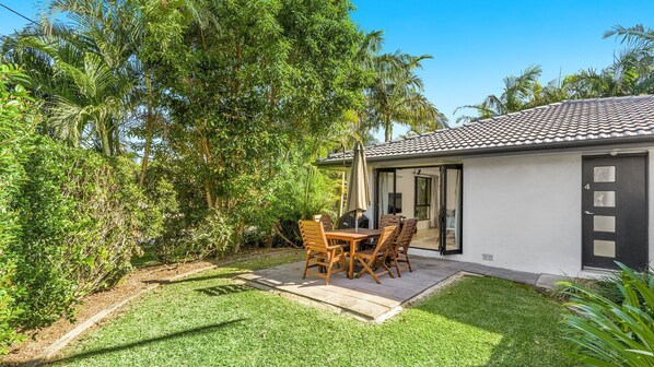 A house with a tiled roof, a patio with a table and chairs, and a door with a number. - Byron at Clarkes - location perfection! Walk everywhere (Byron Bay)