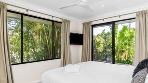 A hotel room with large windows, a flat-screen TV, a neatly made bed, and a ceiling fan. - Byron at Clarkes - location perfection! Walk everywhere (Byron Bay)