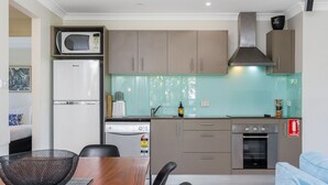 A compact kitchen with a microwave, refrigerator, stove, and oven. There is a dining area with a table and chairs. - Byron at Clarkes - location perfection! Walk everywhere (Byron Bay)