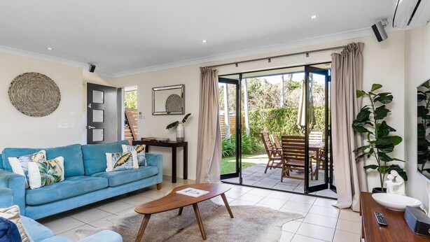 A living room with a blue sofa, a wooden coffee table, and a sliding glass door leading to an outdoor patio with a table and chairs. - Byron at Clarkes - location perfection! Walk everywhere (Byron Bay)