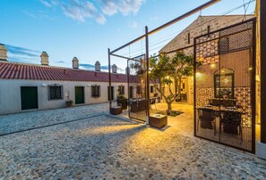 A courtyard with cobblestone flooring, a metal gate, and a building with a tiled roof.
