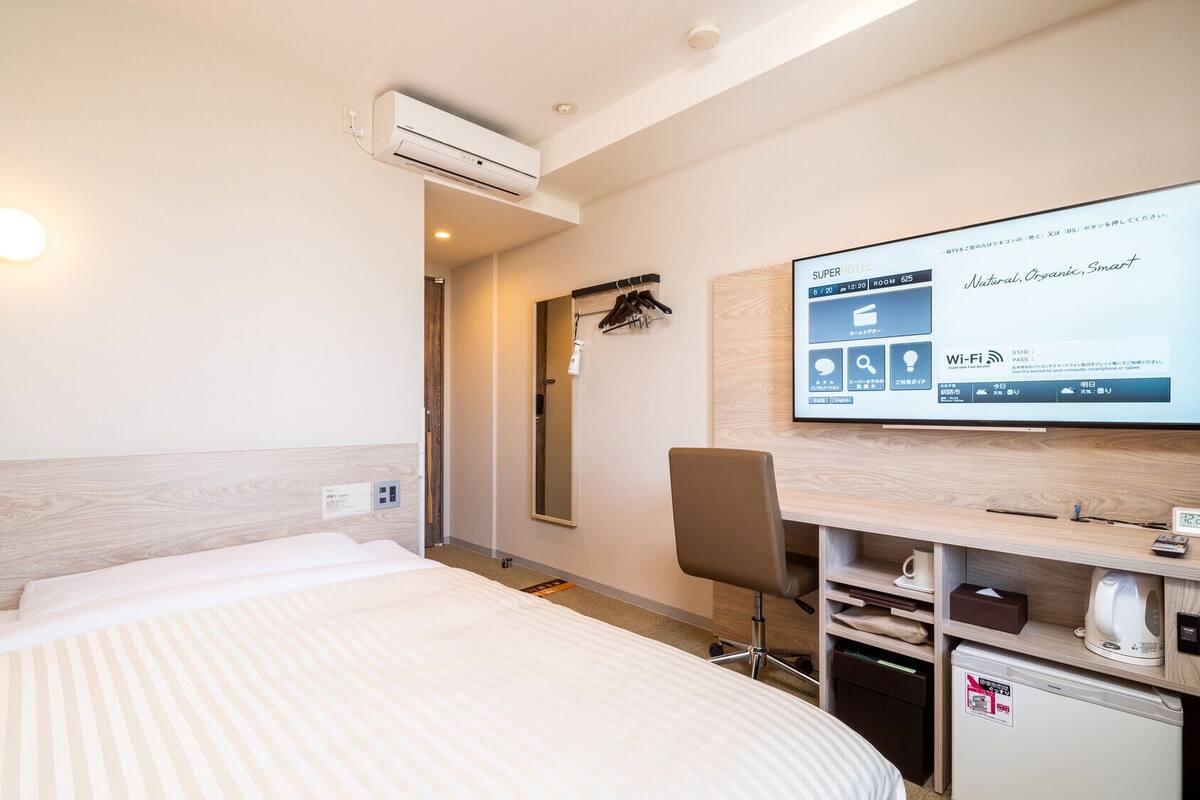 A hotel room with a bed, a desk with a computer, an air conditioner, and a TV displaying hotel information.