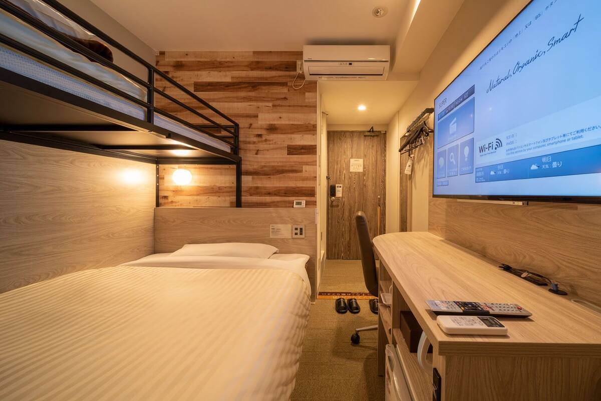 A compact hotel room with bunk beds, a desk with a computer, and a TV displaying a room service menu.