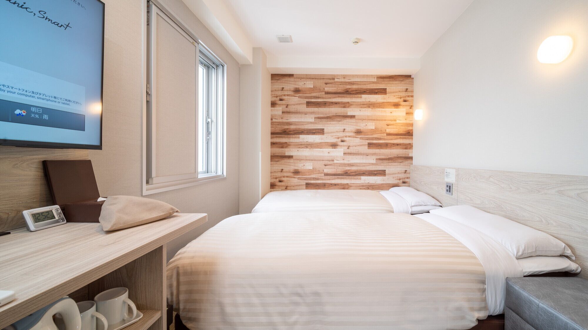 Une chambre d’hôtel moderne avec un panneau mural en bois, un lit avec une literie blanche, un bureau avec un ordinateur portable et une horloge numérique.