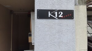 A black sign with white text reading "K12 Kyoto" mounted on a textured wall. - Guest house Shijo K12 (Kyoto)