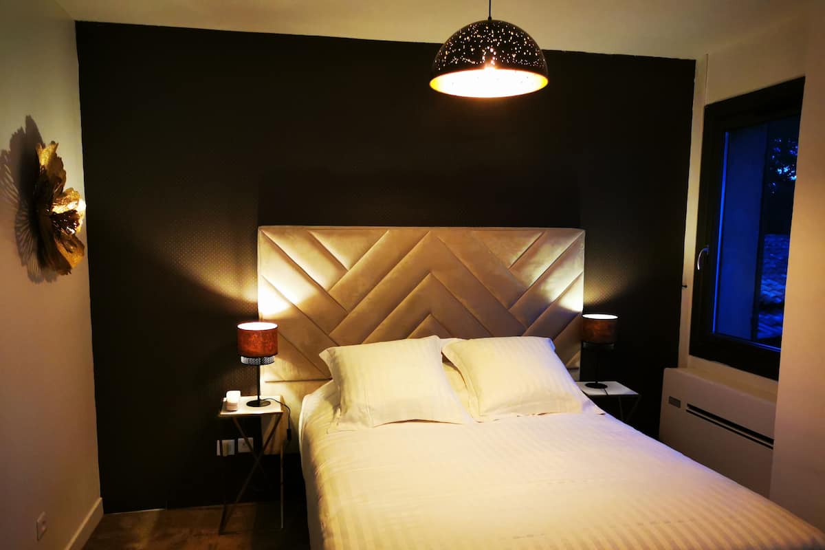 Un lit bien fait, avec une grande tête de lit rembourrée, dans une pièce à la lumière tamisée.