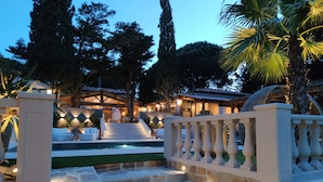 A well-lit outdoor area with stone steps leading to a covered seating area, surrounded by trees and a pool. - La Villa Dune, Hôtel & Spa  (Gassin)