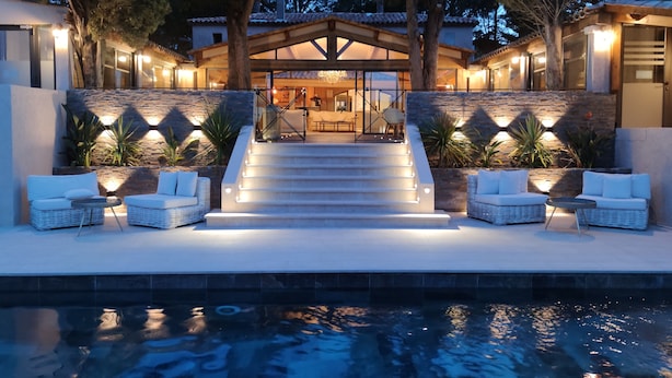 A modern outdoor pool area with steps leading to a covered seating area, surrounded by stone walls and potted plants. - La Villa Dune, Hôtel & Spa  (Gassin)