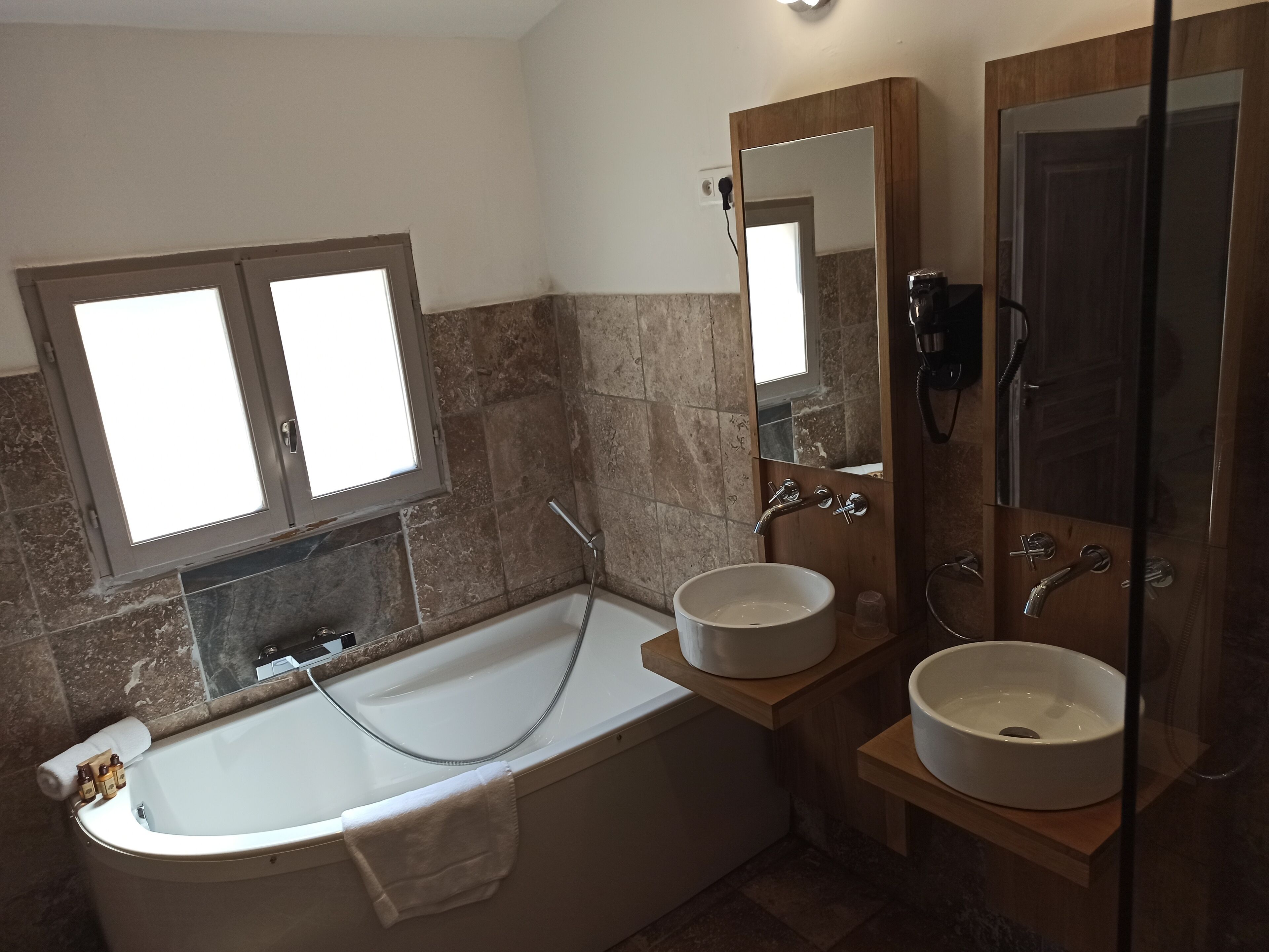 A bathroom with a bathtub, two sinks, a large mirror, and a window.