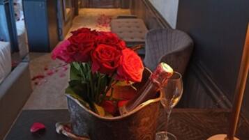 A hallway with a wooden door at the end, a small table with a vase of red roses, a bottle, and a glass.