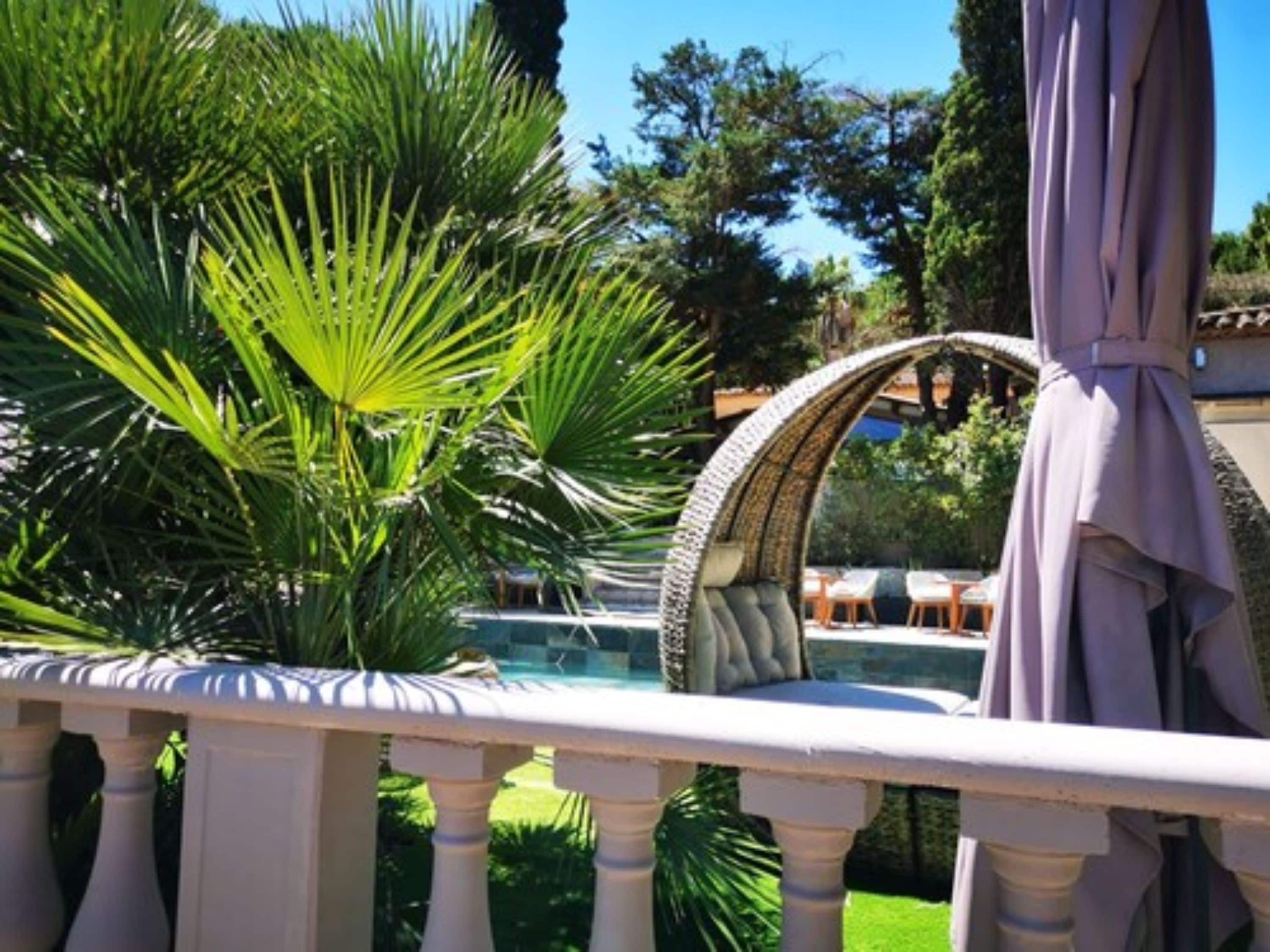 Un espace aménagé au bord de la piscine, agrémenté d’une balustrade blanche, d’une arche en pierre et d’une végétation luxuriante.