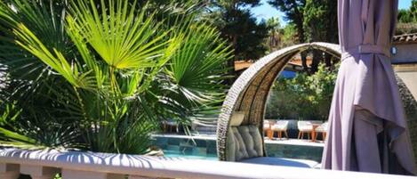 A poolside area with a white balustrade, a stone archway, and lush greenery.